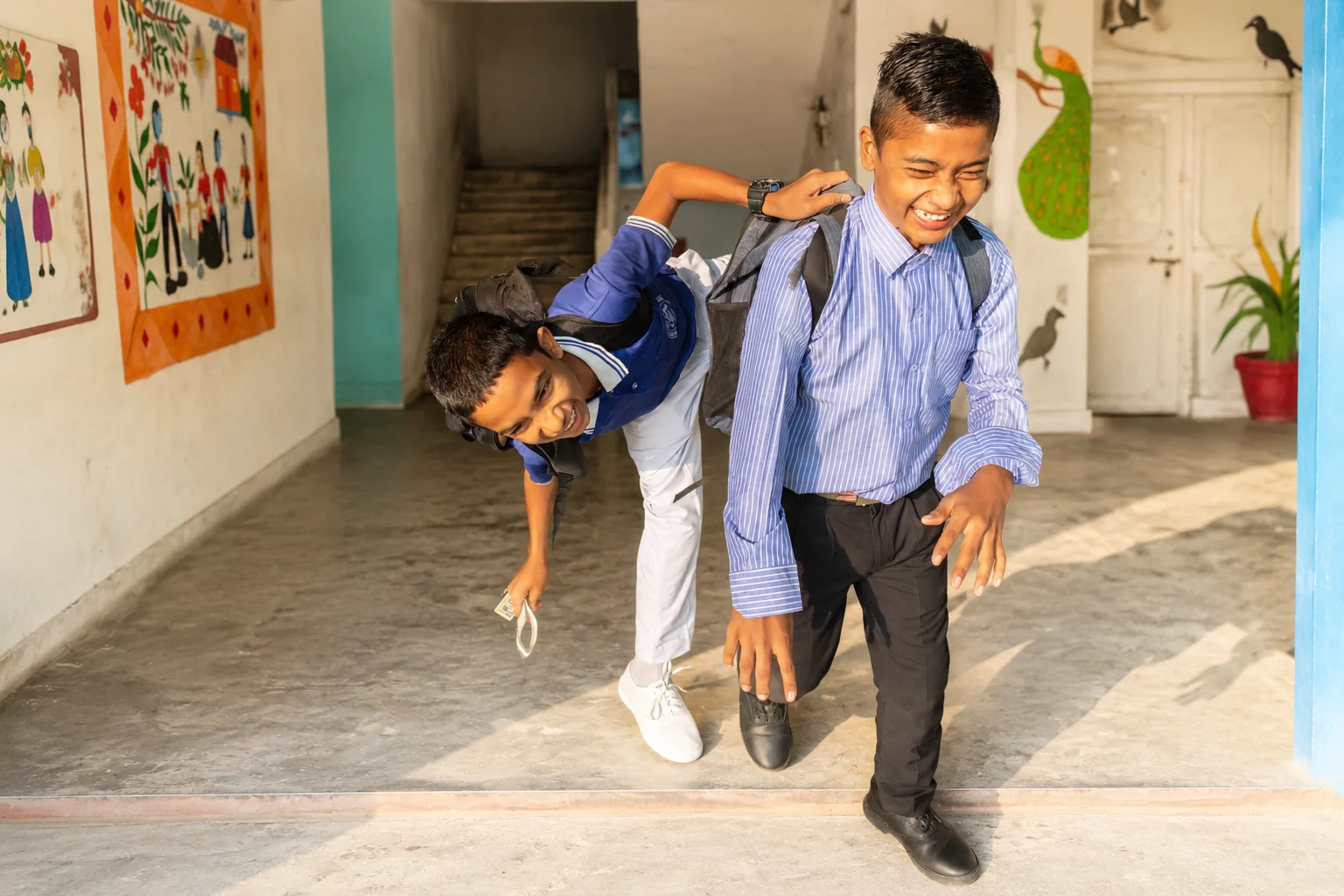 Two schoolboys laughing as they run along a school corridor