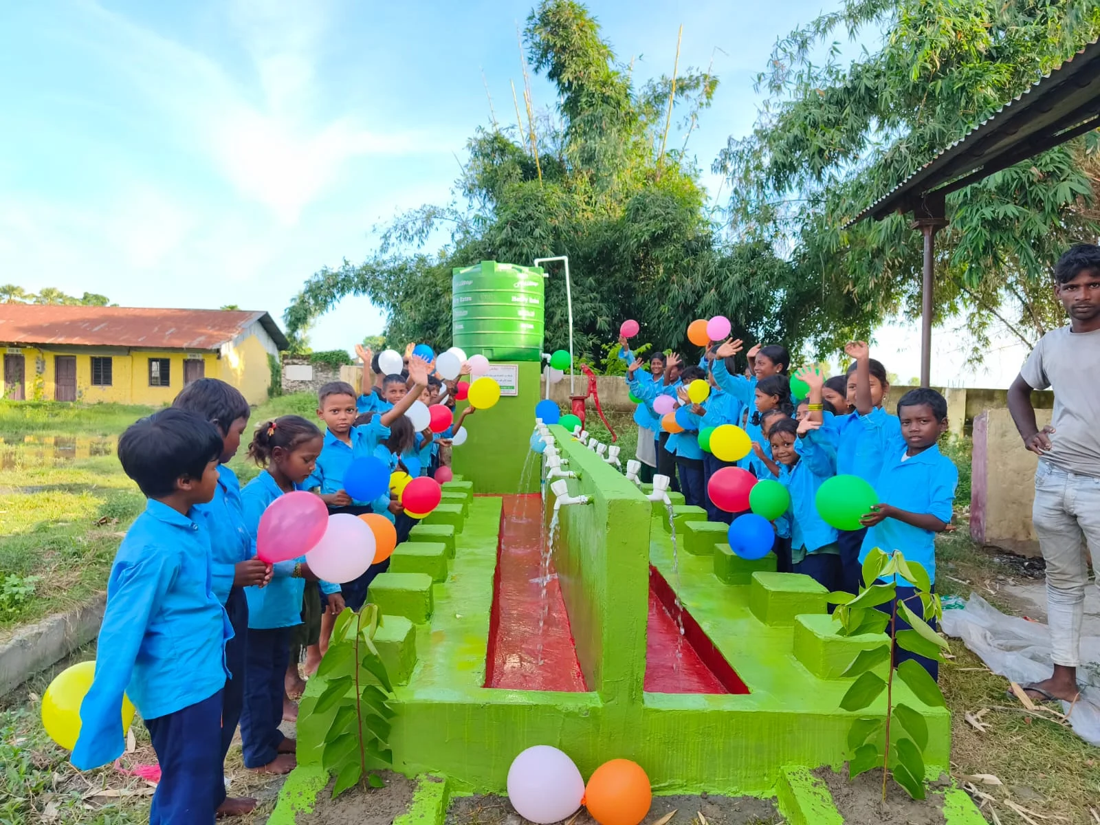 Children in blue uniforms gathered beside a decorated water point outside a school
