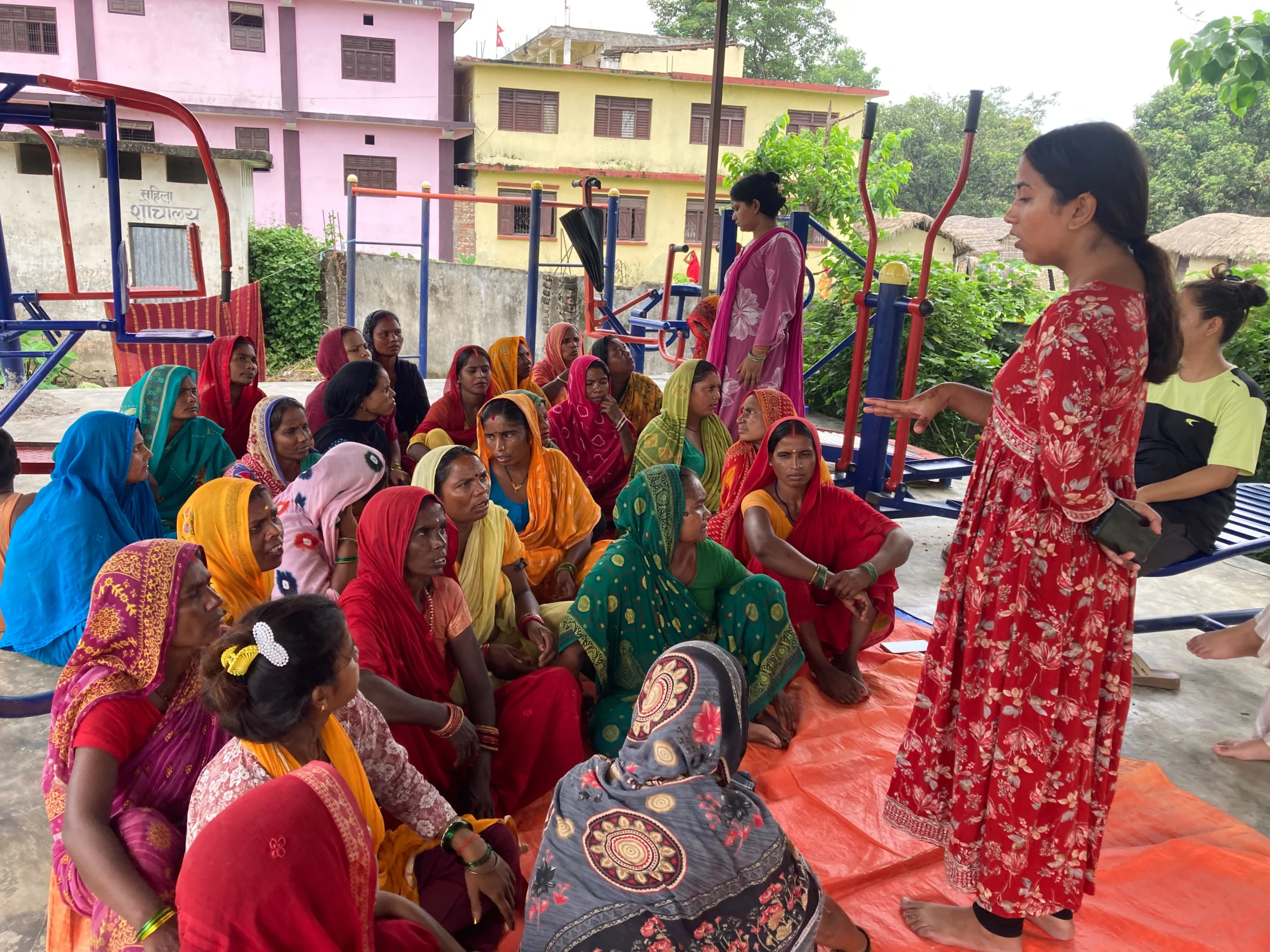 Woman speaking to a group of women sitting on the ground outdoors