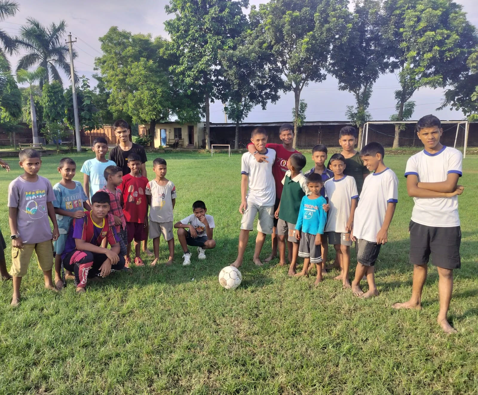 Group of children and adults standing on a grass field with a football
