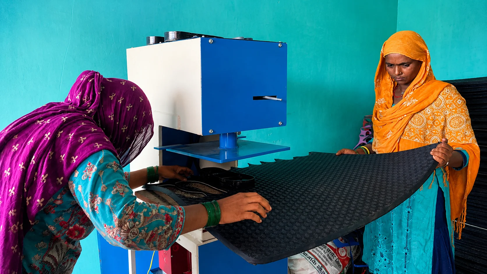 Two women working with fabric and a machine in a workshop