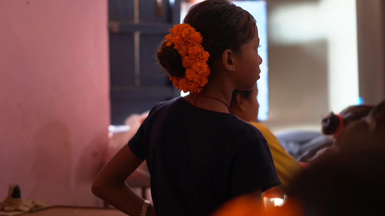 Our Sansar is led by a dedicated team Girl with an orange flower in her hair looking across a room