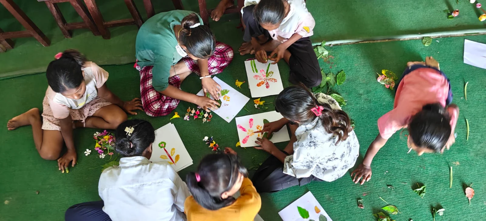Children drawing and playing on a green mat, seen from above