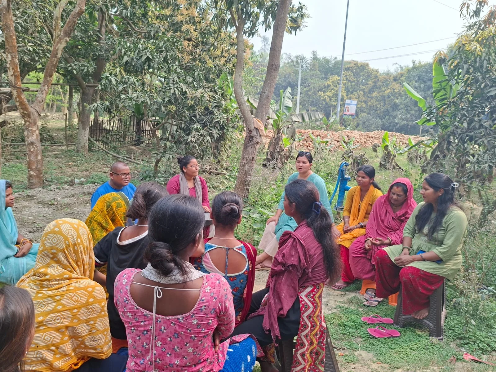 Women and girls sitting in a circle at an outdoor community meeting