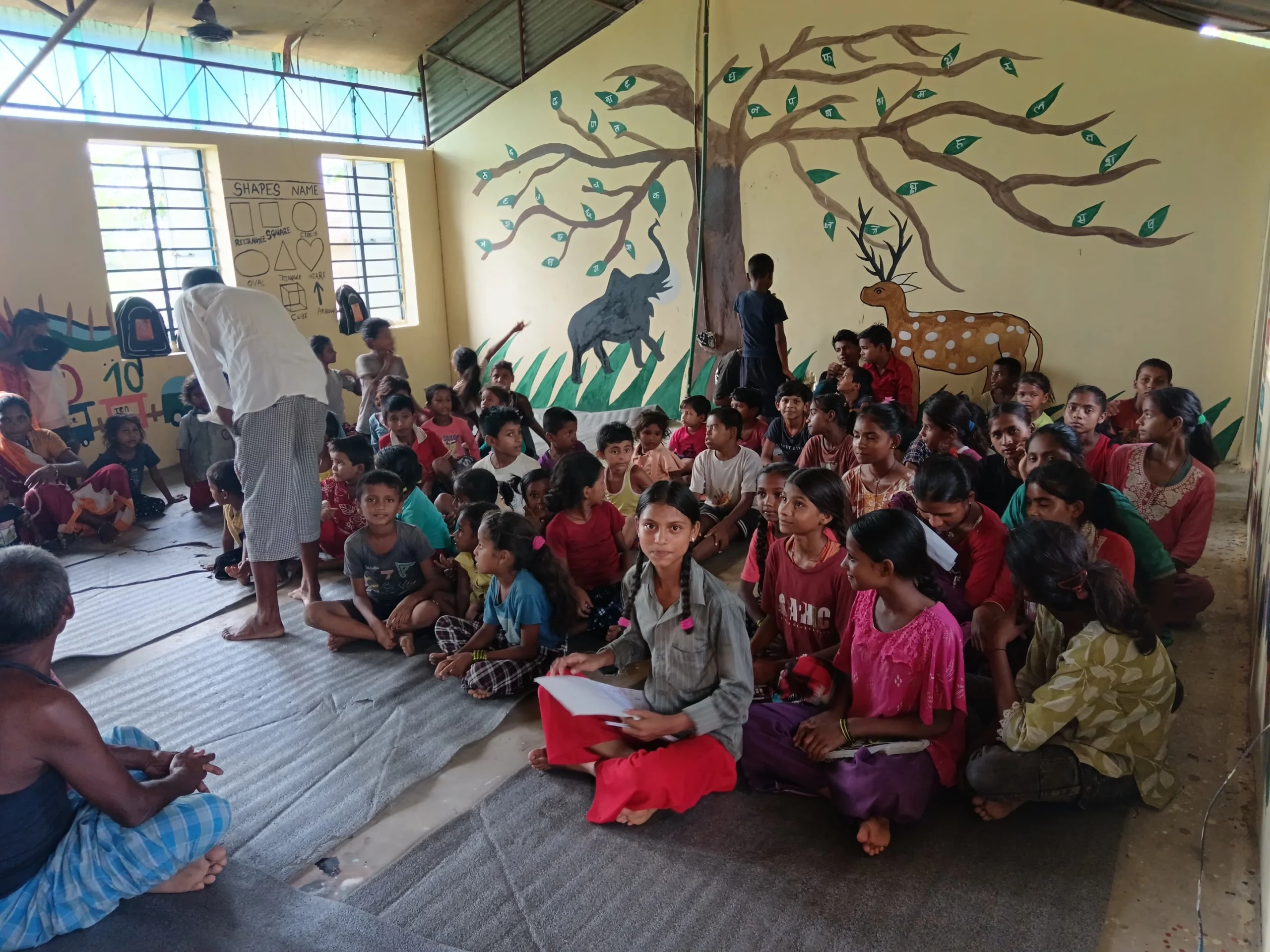 Working Together Large group of children sitting together in a classroom with a painted tree on the wall