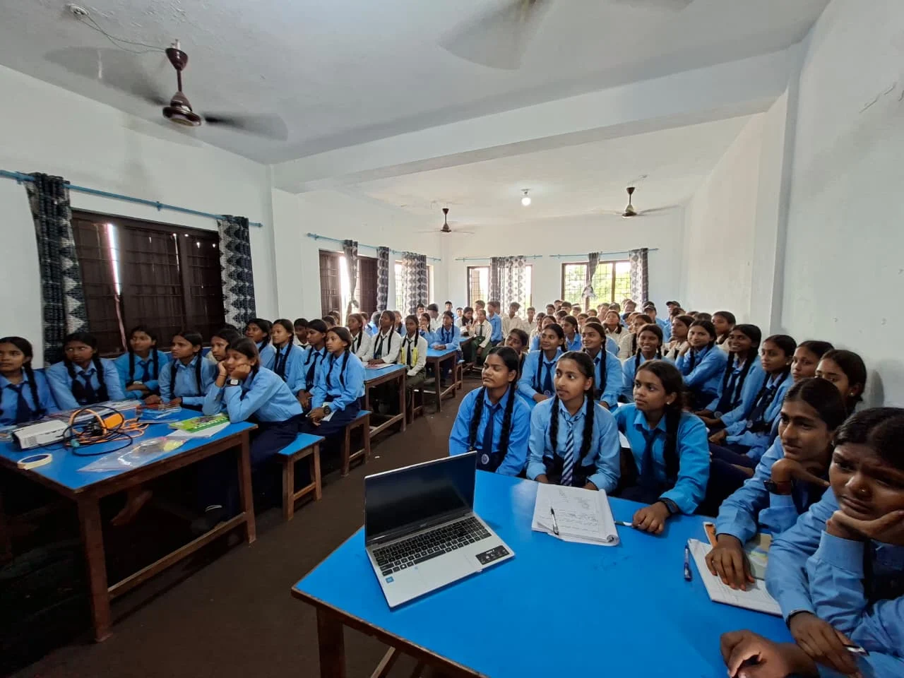 Girls in blue uniforms sitting at desks with laptops in a classroom